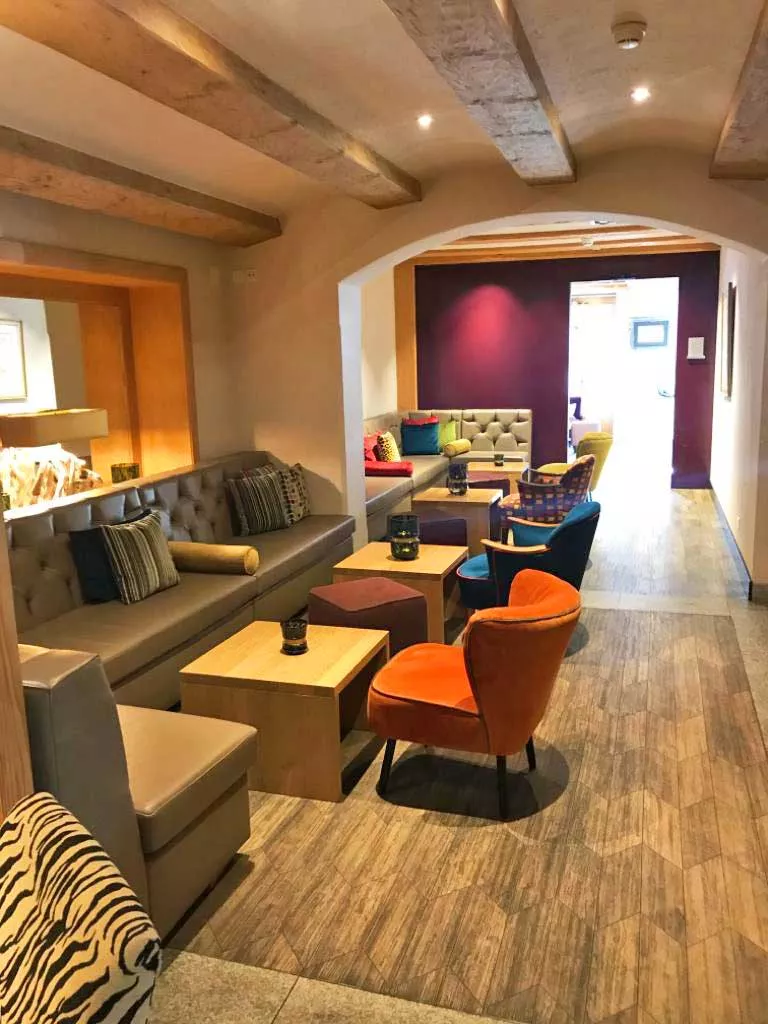 Fertig eingerichteter Lounge-Bereich mit Holzboden, gepolsterten Bänken und farbigen Sesseln nach Renovation