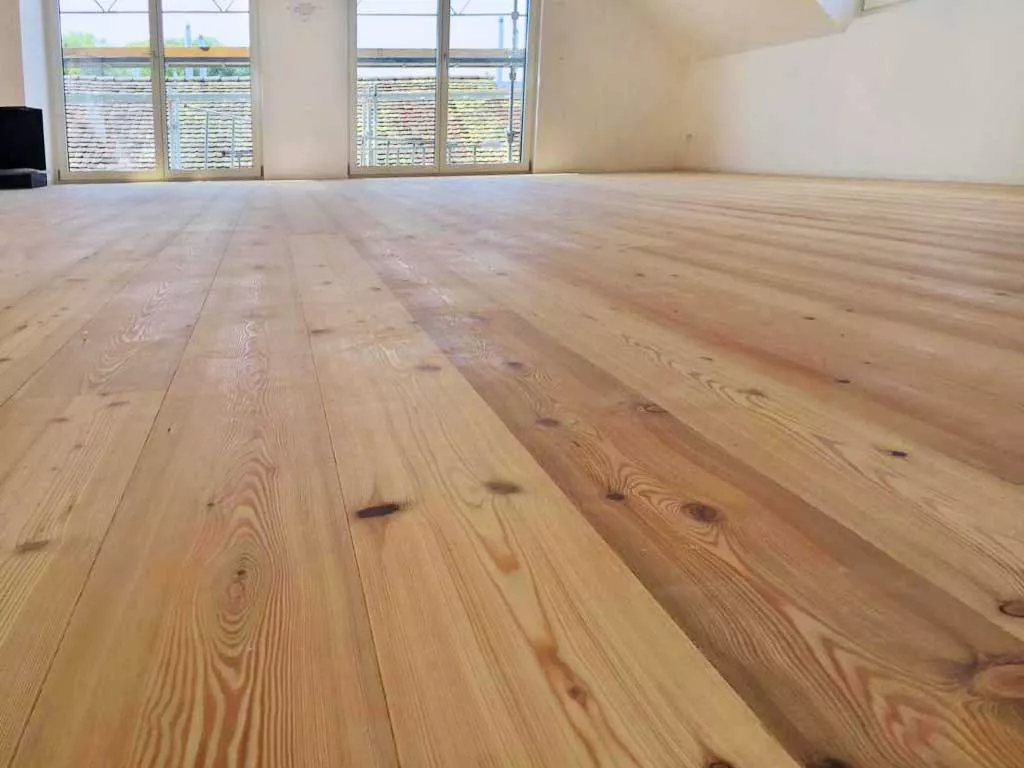 Frisch verlegter und geschliffener Holzdielenboden in einem hellen Dachraum mit grossen Fenstern